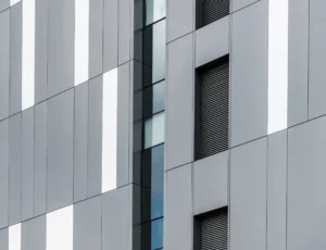 A modern vertical building facade featuring rectangular light grey and dark grid panels.