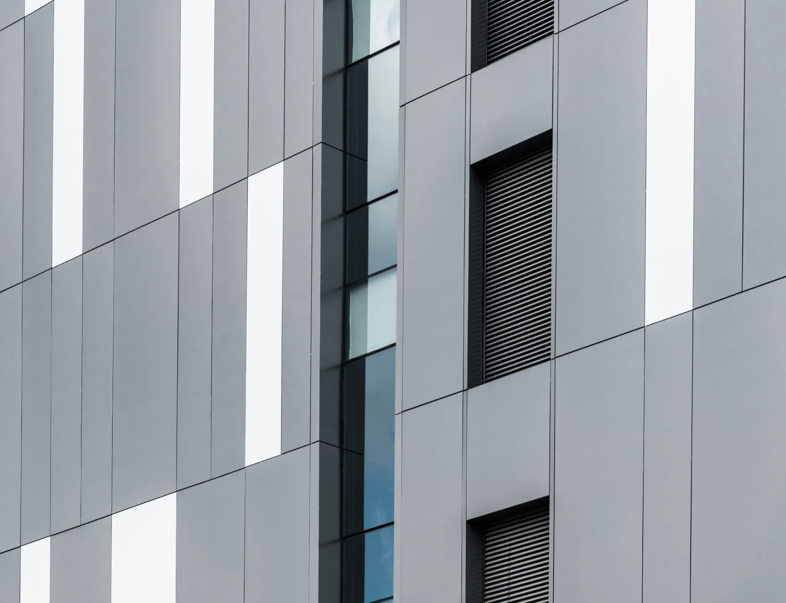 A modern vertical building facade featuring rectangular light grey and dark grid panels.